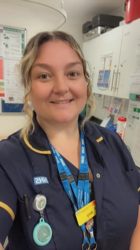 Caucasian woman with blonde hair, wearing dark blue NHS uniform, smiling at the camera