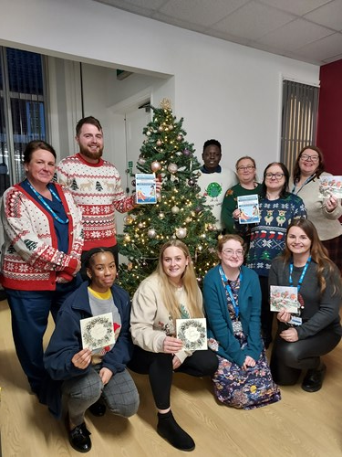 Team of people around a Christmas tree holding Christmas cards. 
