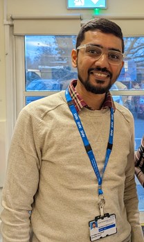 Indian doctor wearing glasses and a light coloured jumper, smiling at the camera