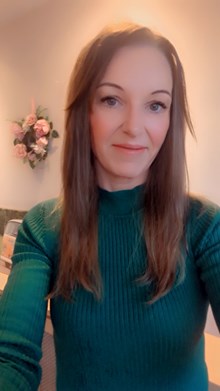 Caucasian woman wearing a green top, light brown shoulder length hair smiling at the camera