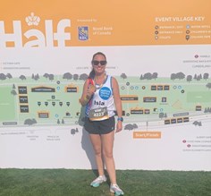 Woman smiling at the camera holding a medal at the end of a race.