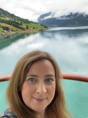 Woman standing in front of a lake smiling at the camera.