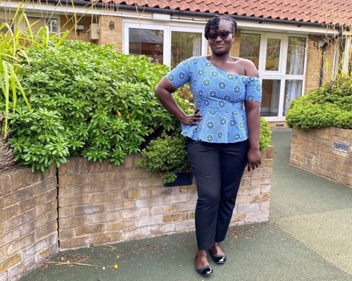 Photo of Linda Aidoo, wearing a light blue top, black trousers, smiling.