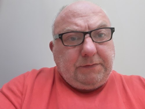 Simon Cross, wearing an orange top, wearing glasses.
