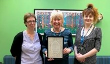 Three women smiling at the camera. The middle woman is holding the award.