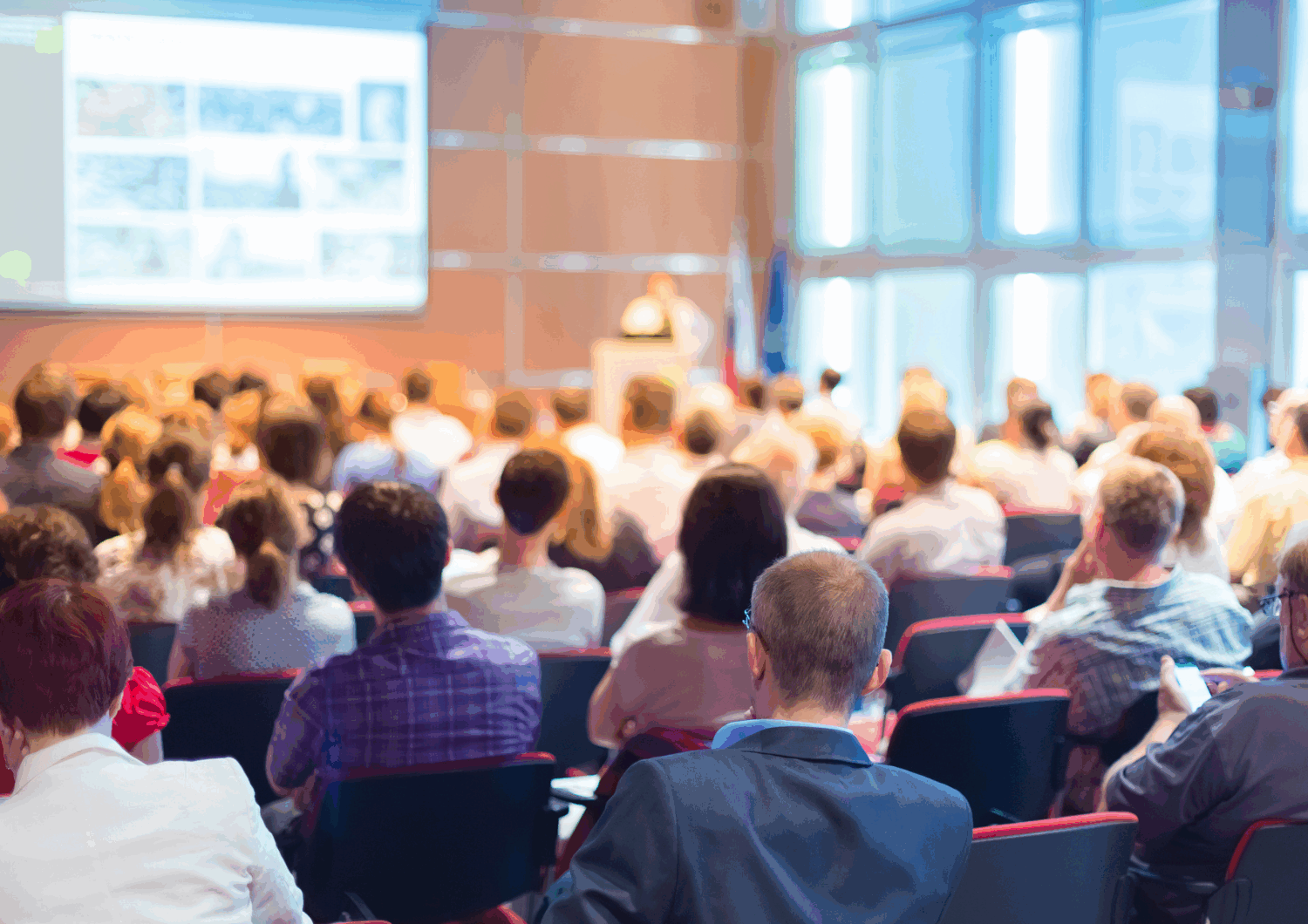room filled with people attending a meeting looking and listening to a presentation.