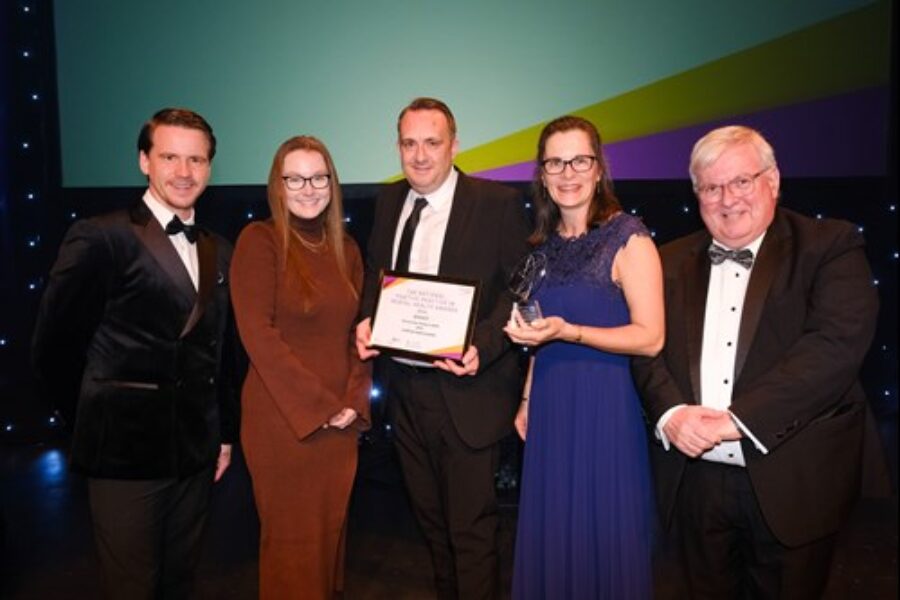 Three men and Two women smiling at a camera holding their team's award.