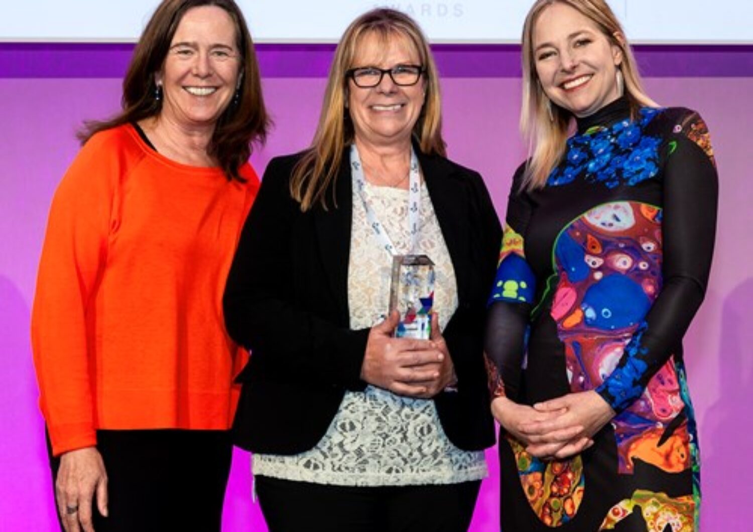 Three women smiling at the camera with Debbie holding her award
