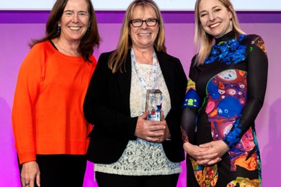 Three women smiling at the camera with Debbie holding her award