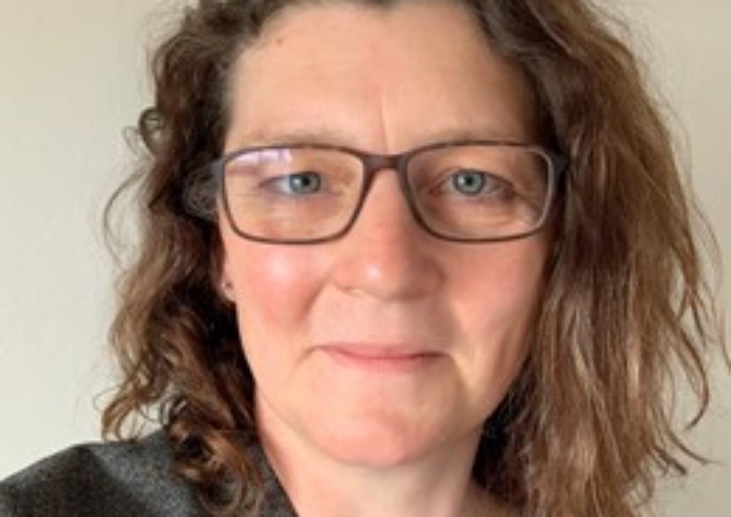 Woman with brown shoulder length hair, wearing glasses, smiling at the camera