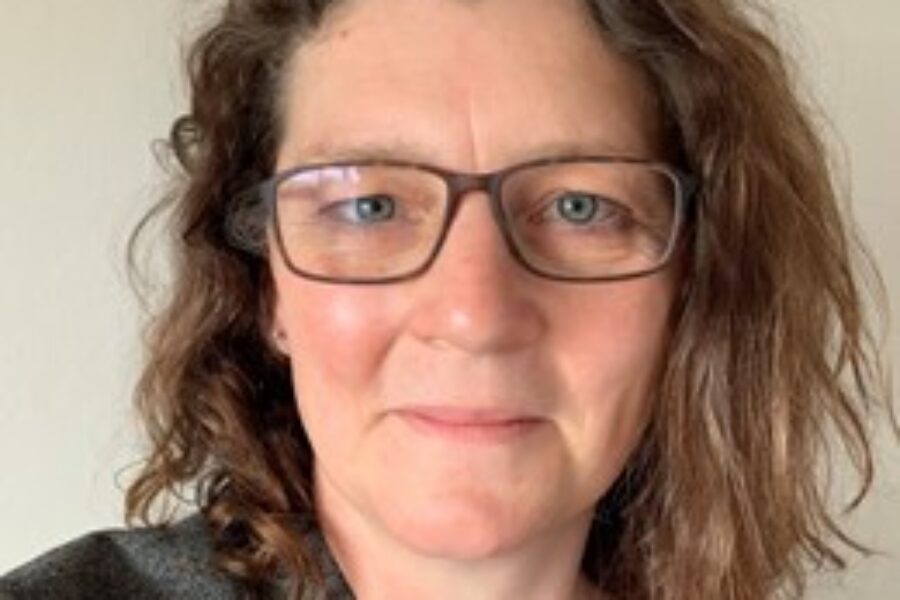 Woman with brown shoulder length hair, wearing glasses, smiling at the camera