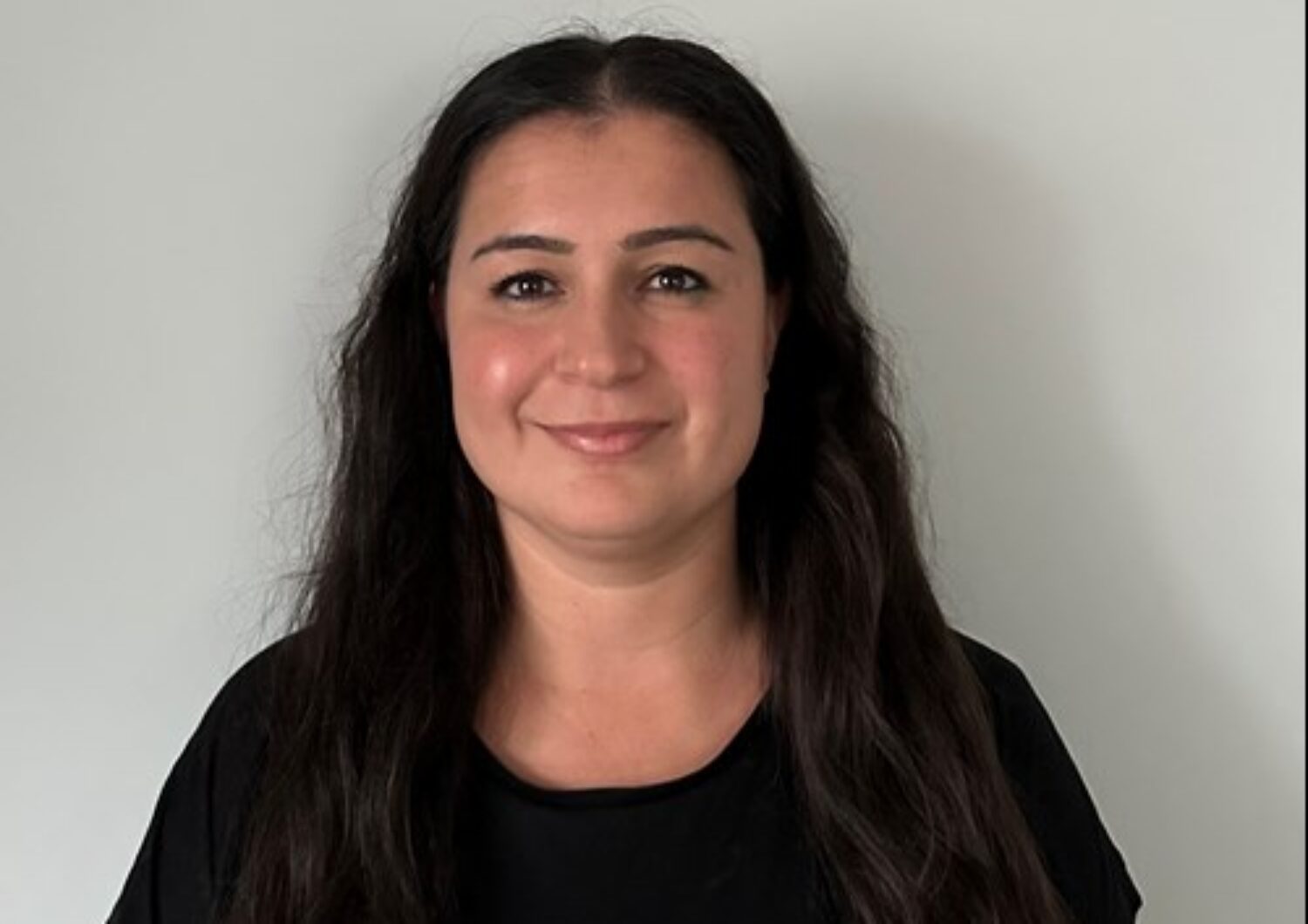 Nursac Durmus, long black hair, wearing a black top, smiling at the camera.